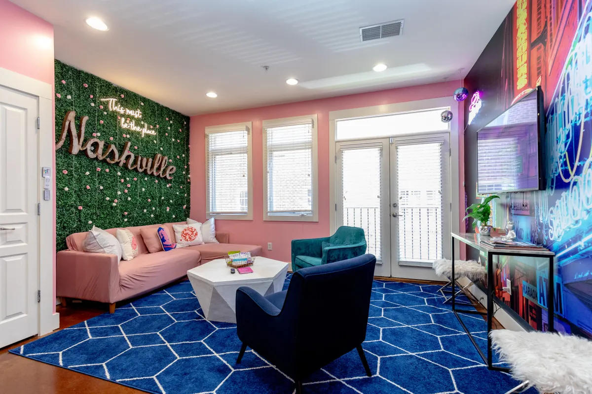 This interior image features a bright living area with a green wall adorned with a 'Nashville' sign, a playful pink sofa, blue armchair, and a colorful coffee table. The decor is festive and welcoming, perfect for group photos, pre-party gatherings, or relaxing in style after a day out.