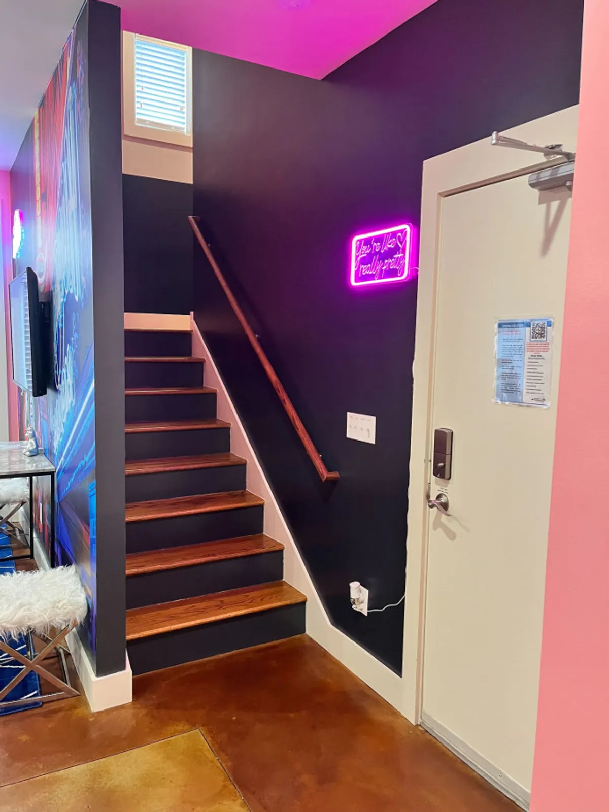 An interior shot highlighting the staircase leading to another level, adorned with playful neon decor and modern wall art. The scene suggests a lively, multi-story living environment with space to both relax and socialize.