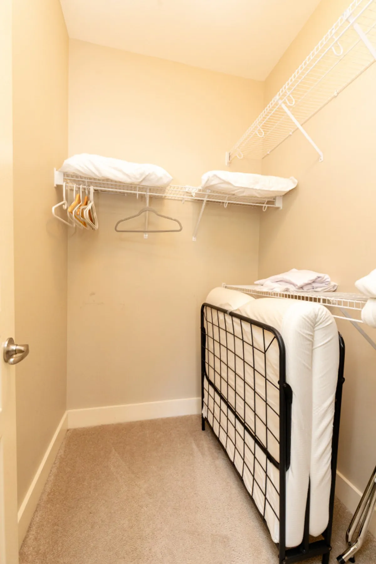 The scene focuses on practical storage: shelves filled with linens, a fold-away bed, and ample hangers. The space is tidy and organized, emphasizing convenience for guests who need extra bedding or flexible sleeping arrangements.