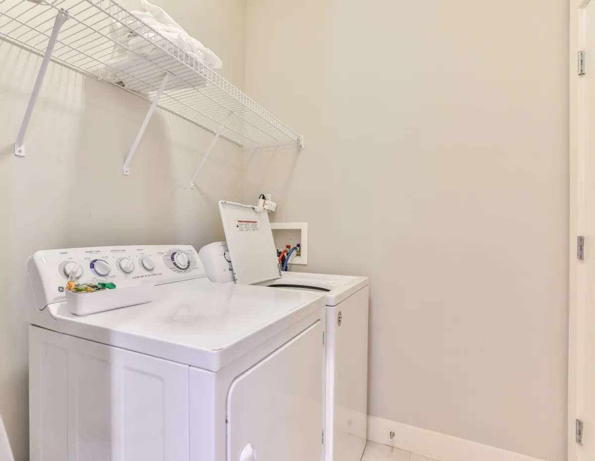 A tidy laundry area featuring a washing machine, dryer, and neatly arranged towels on a shelf. The ambiance is clean and practical, emphasizing convenience and order.