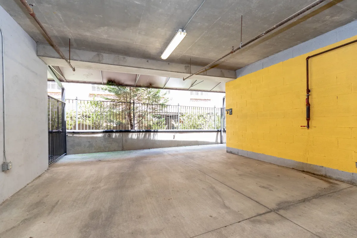 A practical garage space with yellow walls, exposed concrete, and visible lighting fixtures. The area is designed for secure vehicle parking and includes storage options, highlighting convenience and safety for urban explorers.
