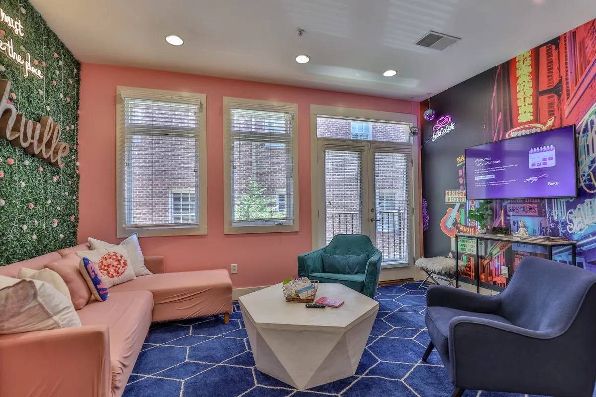 A playful and welcoming seating area with a pink wall featuring 'Nashville' lettering, a geometric coffee table, and colorful seating options. This area exudes a lively social vibe, perfect for casual gatherings or themed celebrations.