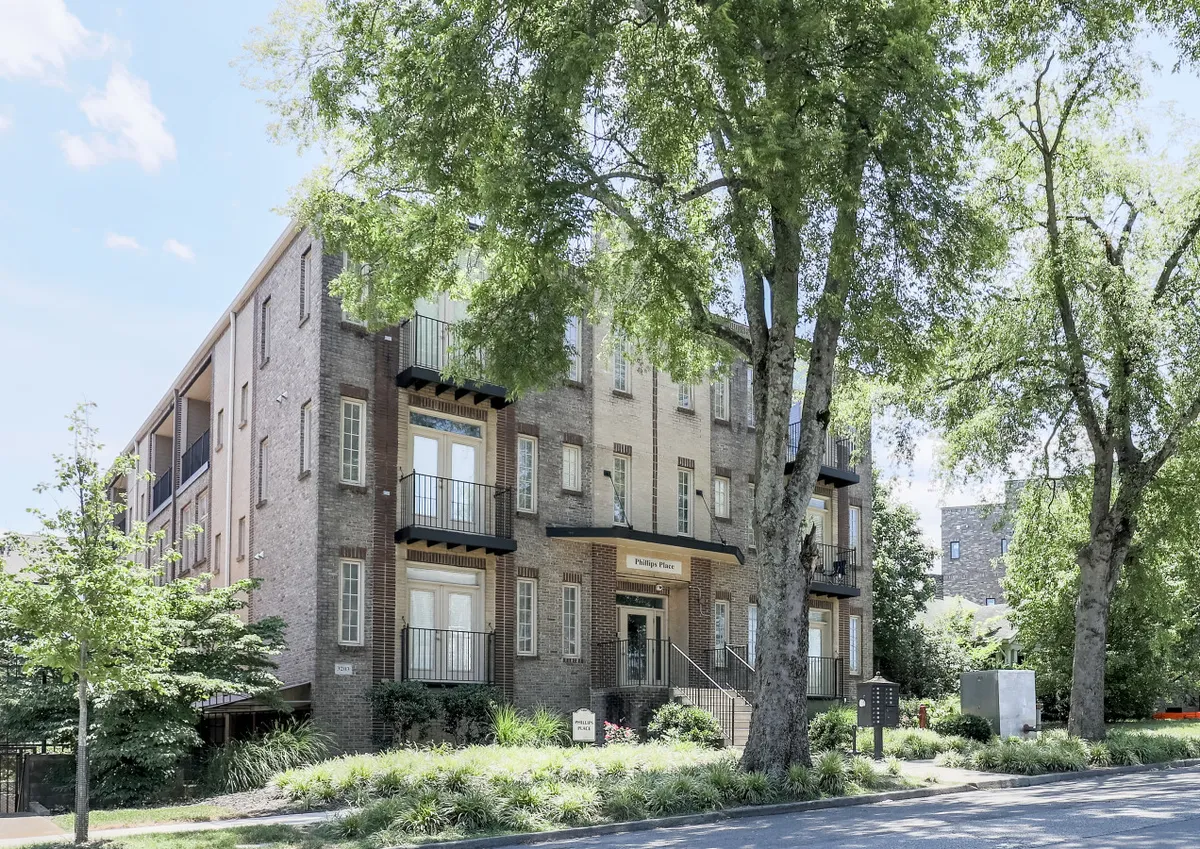 This image showcases the brick facade of the building, complete with balconies and a welcoming entrance surrounded by greenery. The space hints at areas for guests to relax outdoors or gather with friends before heading out to experience Nashville.