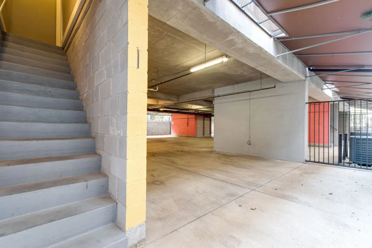 A view of the condo's secure garage parking area, featuring a modern staircase, concrete walls, open space, and a visible security gate. The image conveys ease of access and an urban, practical atmosphere.