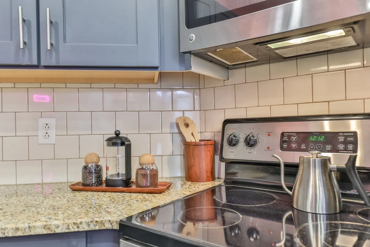 A warm kitchen scene featuring a granite countertop, stainless steel stove, French press, wooden utensils, and decorative jars. The setup is clean and inviting, ideal for preparing family breakfasts or enjoying coffee together before heading out for adventures.